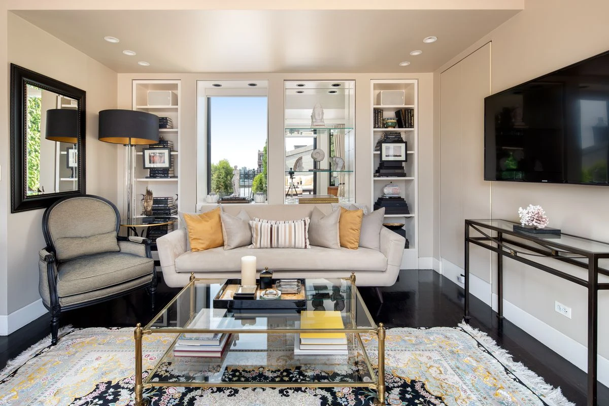 A room with a beige sofa, glass coffee table, and built in shelves.