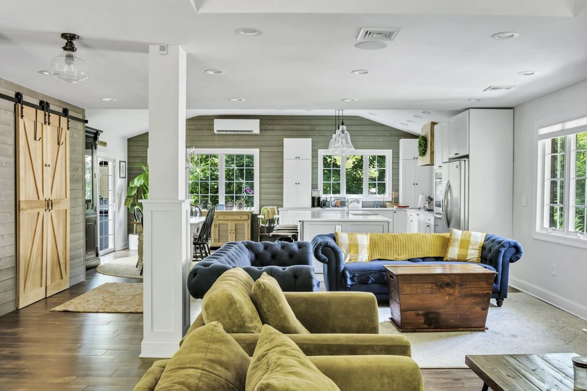 A living room with hardwood floors, large windows, white walls, a column, and several couches.
