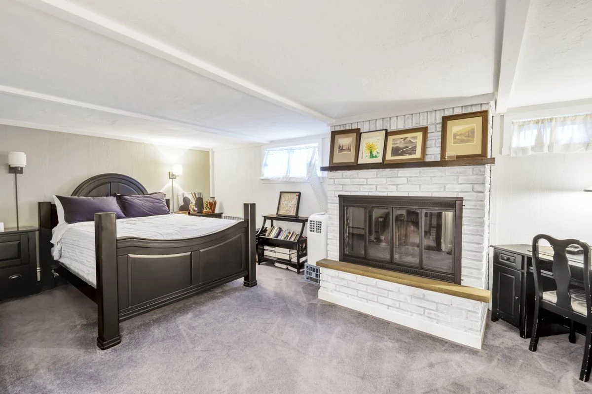 A basement bedroom with a fireplace, a large bed, and a wooden desk.